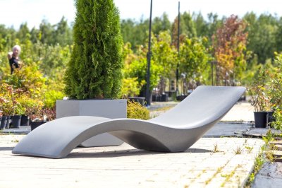 Серый шезлонг эргономичной формы на деревянном настиле с зелёными растениями